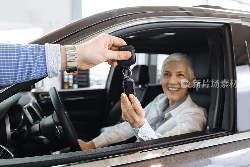 一位年长的女士从汽车销售员那里拿到了一辆新车的钥匙