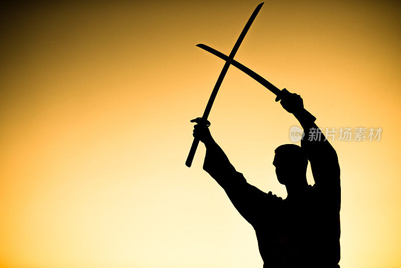 剪影的武术艺术家抱着两个武士刀一起在日落。