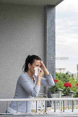 有过敏症的年轻女子在阳台上晾湿衣服