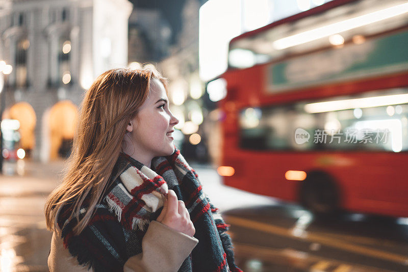 晚上在皮卡迪利广场，一个女人看着一辆红色的伦敦公共汽车