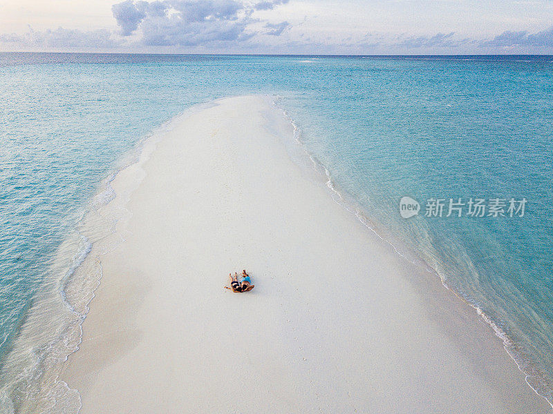 一对年轻的成年夫妇一起躺在马尔代夫碧绿的沙滩上