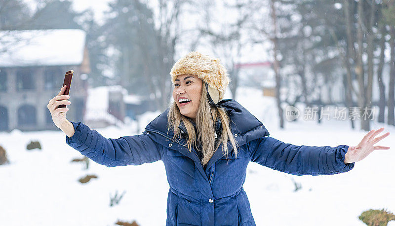 一名身穿蓝色外套的女子在雪山里用手机自拍