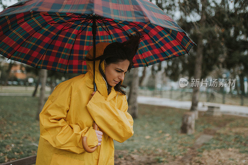 穿着黄色雨衣的年轻女子在公园里度过雨天