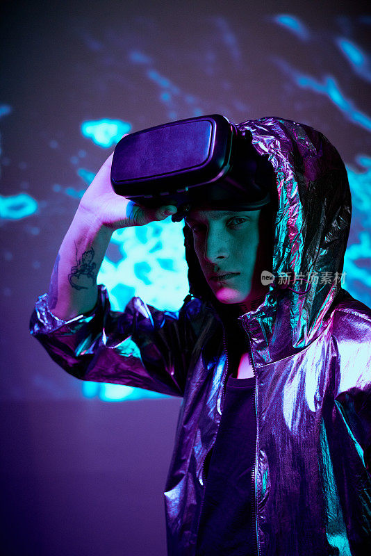 肖像严肃的年轻男性VR玩家在兜帽夹克脱下虚拟现实眼镜