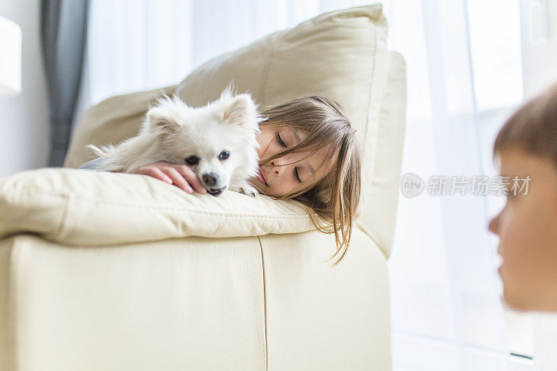 可爱的女孩躺在沙发上和她的狗在客厅在家里库存照片