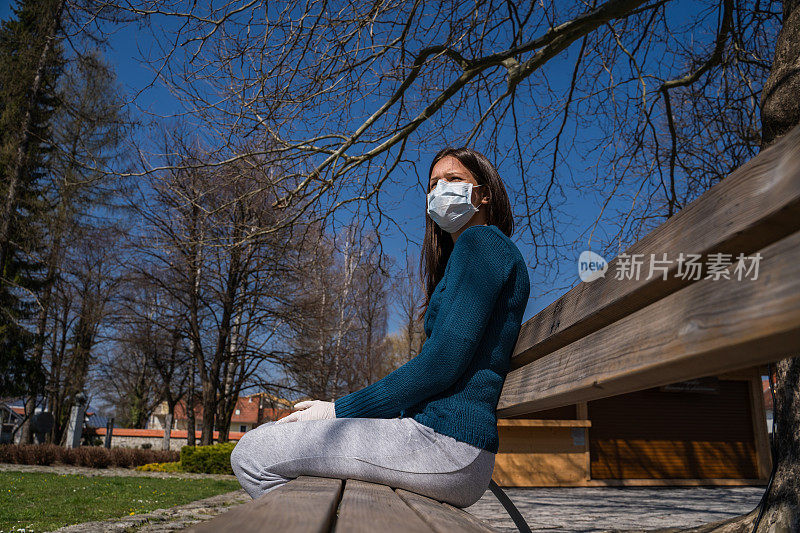 戴面具的孤独女人坐在公园长椅上的照片