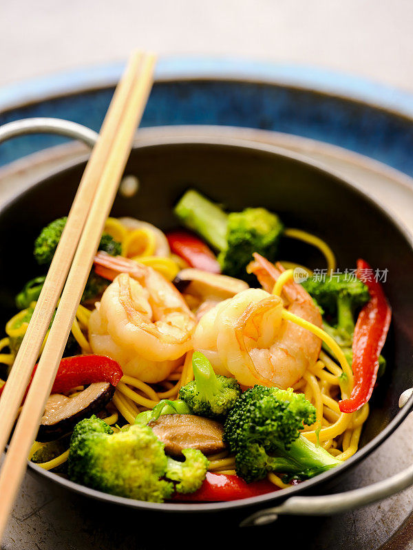 新鲜的亚洲炒虾与蔬菜和面条在一个个人服务的锅，筷子放在锅上。