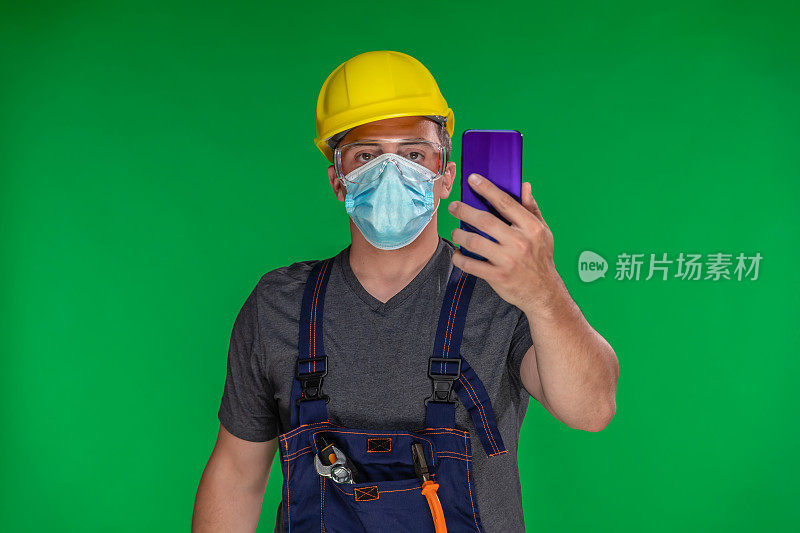 建筑工人戴着N95防护面罩和头盔使用智能手机