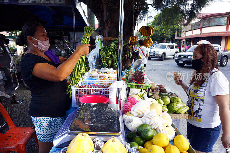 顾客从路边的一个摊贩那里买新鲜的水果和蔬菜