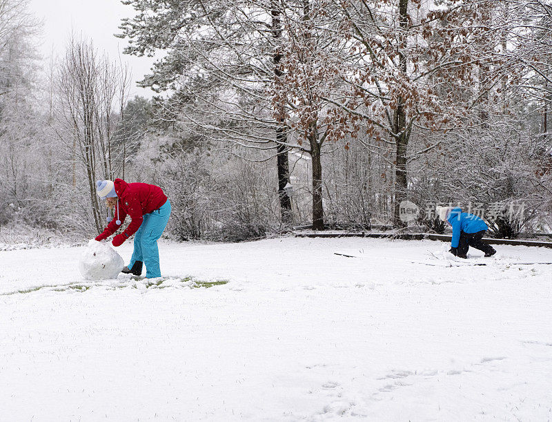一个白人女孩带着一个孩子，一个5岁的女孩，在他们家的院子里堆雪人。