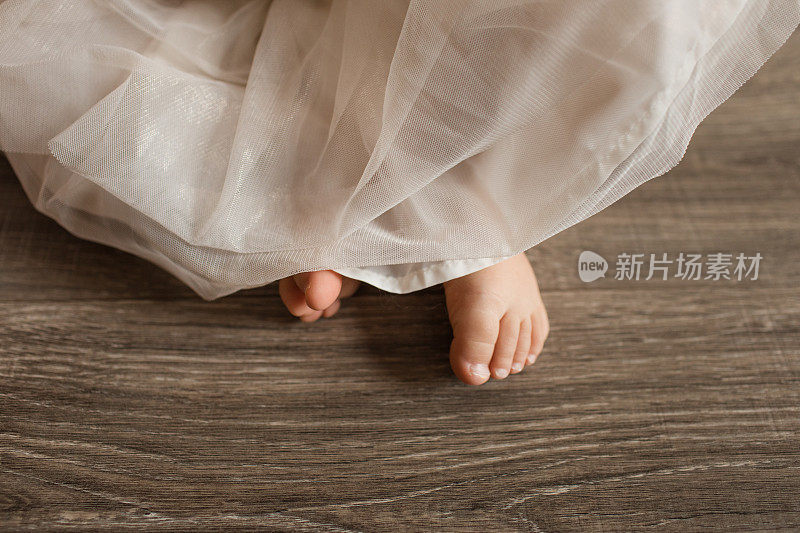 19个月大的小女孩和南瓜坐在木地板上，她的脚从象牙短裙下向外窥视
