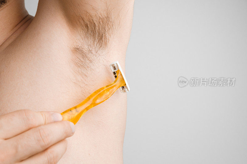 近距离观察，男人用一把黄色剃须刀刮毛腋窝。腋下或腋下未刮毛。脱毛和脱毛程序。身体羞辱的概念