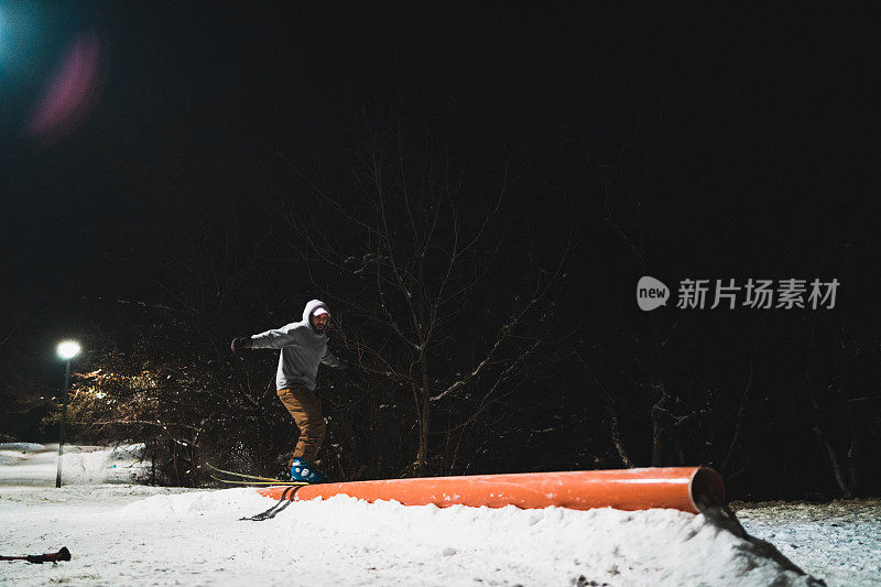 一名冬季滑雪胜地的男性高山滑雪者在晚上跳上了栏杆