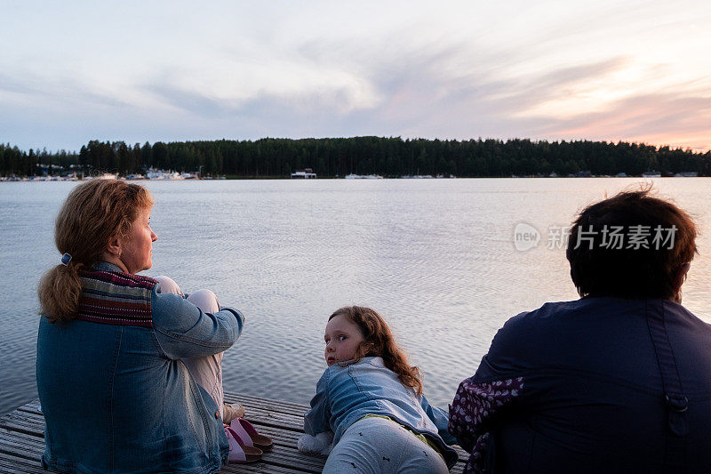 一家人，白人妇女和一个孩子，一个8岁的女孩，看着湖上的日落。