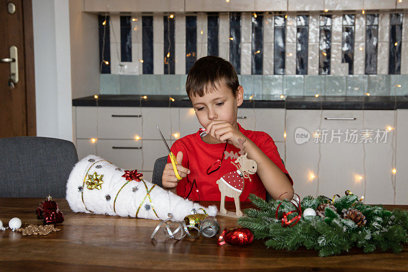 一个可爱的男孩坐在家里的桌子旁，自己动手做圣诞工艺品。新年。手工制作的工作。