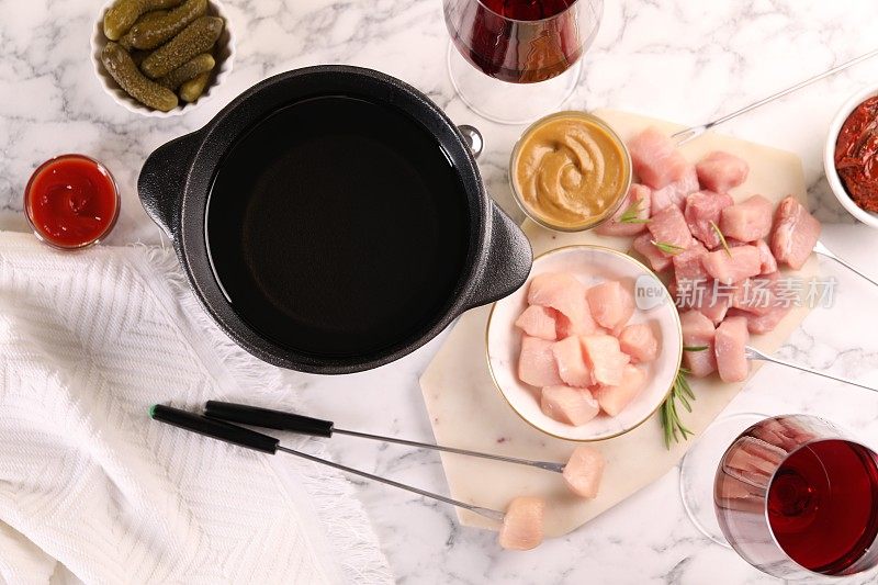 火锅锅用油、叉子、生肉块、红酒杯等产品放在白色大理石桌上，平铺