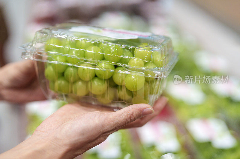 在一个特写镜头中，一个女人的手在杂货店里挑选一盒葡萄