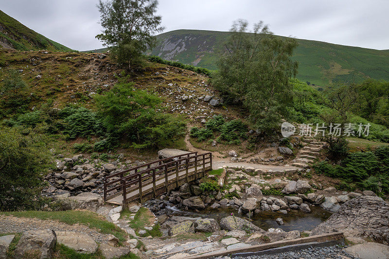 风景如画的人行桥横跨在一个郁郁葱葱的山景溪流-威尔士海岸小径在阿伯瀑布