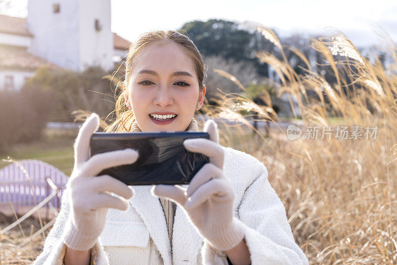 迷人的亚洲女性旅行者休闲布手拍照与智能手机设备，而一日游独自旅行与草地草地迷人的地方日落背景