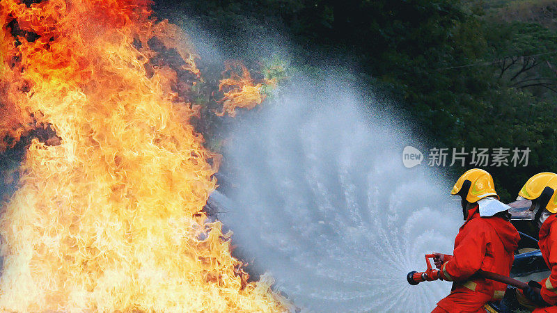 消防救援队员接受灭火器训练。团队合作消防队员使用消防水带化学水泡沫喷雾机与火焰搏斗。消防队员穿安全帽制服