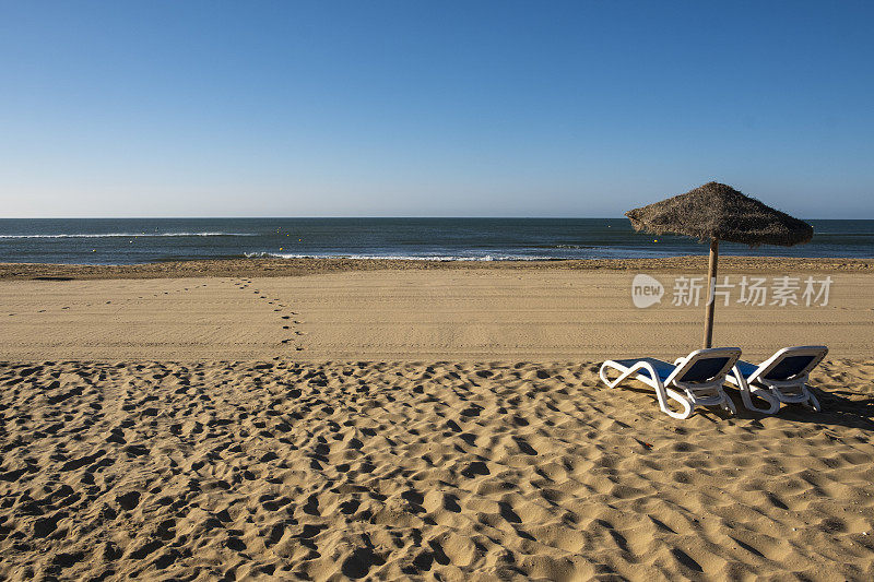 美丽的夏日风景的西班牙海岸，两个太阳躺椅，太阳躺椅和遮阳伞。金色细沙，地平线海景，蓝天，平静放松。鼓舞人心的度假景观。