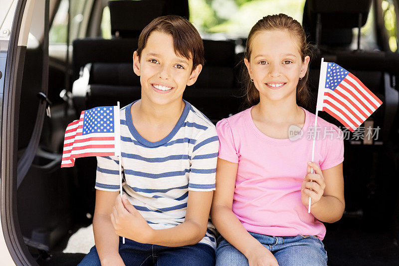 弟弟和妹妹在汽车后备箱里拿着美国国旗