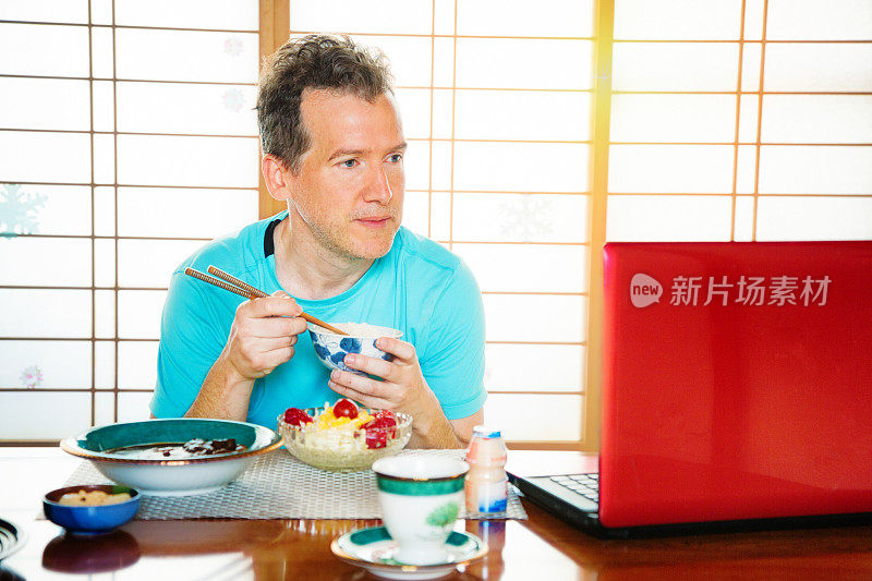 白人游客一边吃日本菜一边在笔记本电脑上看媒体