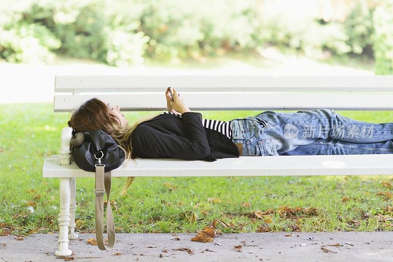 少女躺在公园长椅上发短信