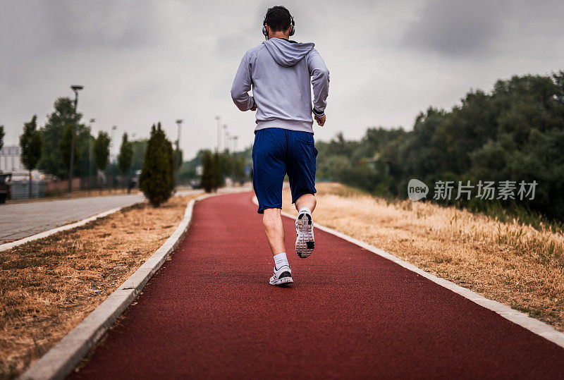 在运动跑道上慢跑的运动员的后视图。