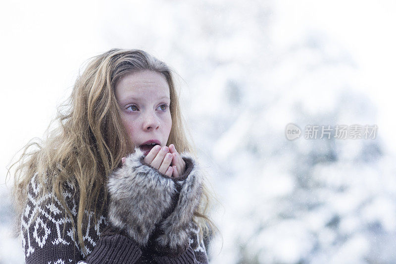 女孩在雪中对着裸露的手指吹气