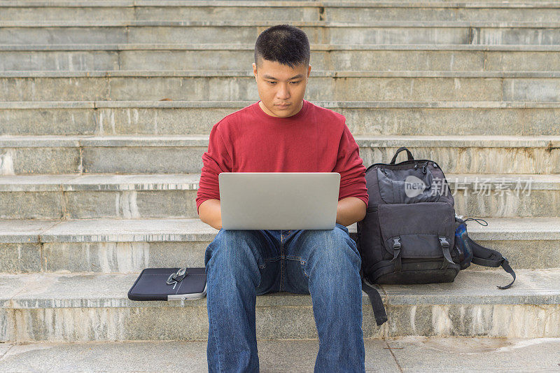 坐在楼梯台阶上使用笔记本电脑的男同学