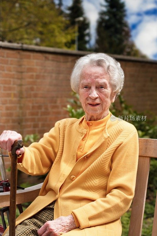 快乐的老妇人拄着拐杖坐在户外