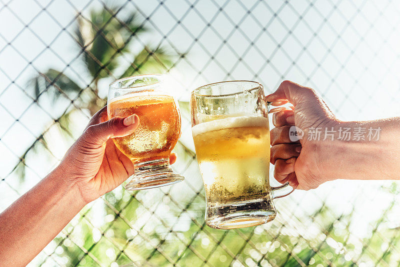 两只手在热带的阳光下用啤酒杯敬酒