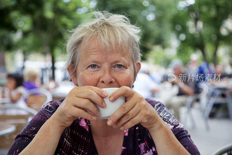 一位年长的女士正在户外咖啡馆喝咖啡。