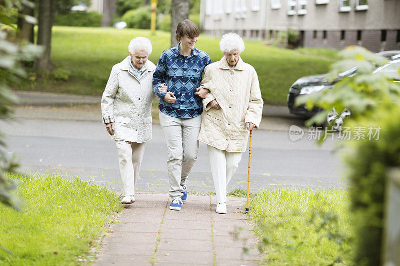 年轻的看护者帮助老年妇女在街上行走