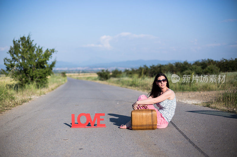 美丽的年轻女子坐在高速公路上提着行李箱