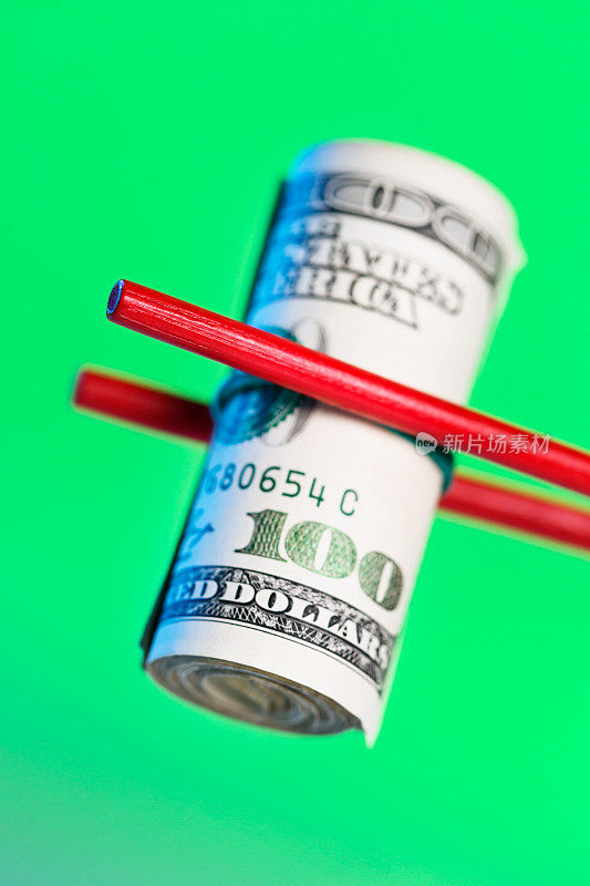 红色的筷子夹起一卷绿色背景的100美元钞票