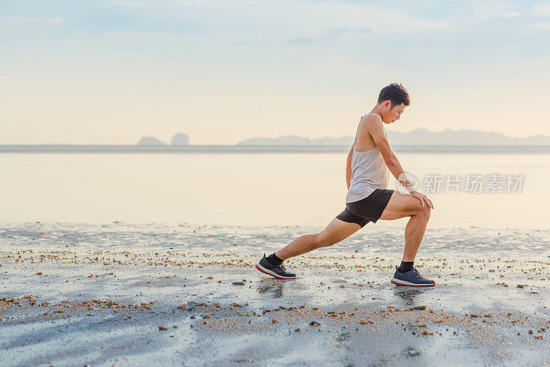 年轻的亚洲男子在海滩上奔跑，夕阳为背景