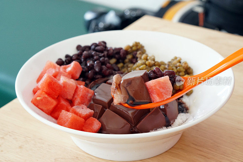 一碗冰镇的巧克力豆腐布丁，上面淋有西瓜、红豆、绿豆和巧克力酱。