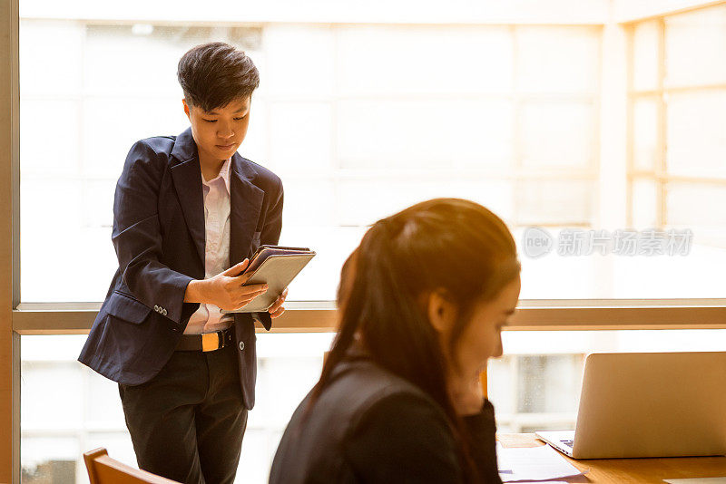 短黑发亚洲商务女性手持智能手机在工作场所与同事