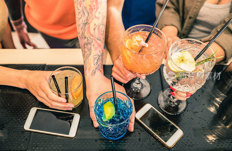 朋友群喝鸡尾酒在时尚酒吧餐厅-高角度的观点，人的手在移动智能手机-社会聚集概念与喝醉的男孩和女孩-生动的蓝绿色滤镜