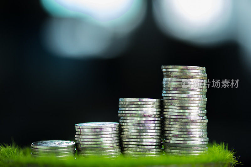 一堆堆硬币在绿草如茵，金融与商业理念浅浅聚焦。