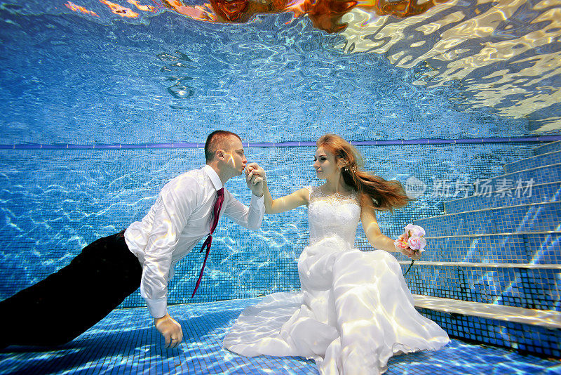 新郎亲吻坐在池底的新娘的手。肖像。水平方向。水下的景色