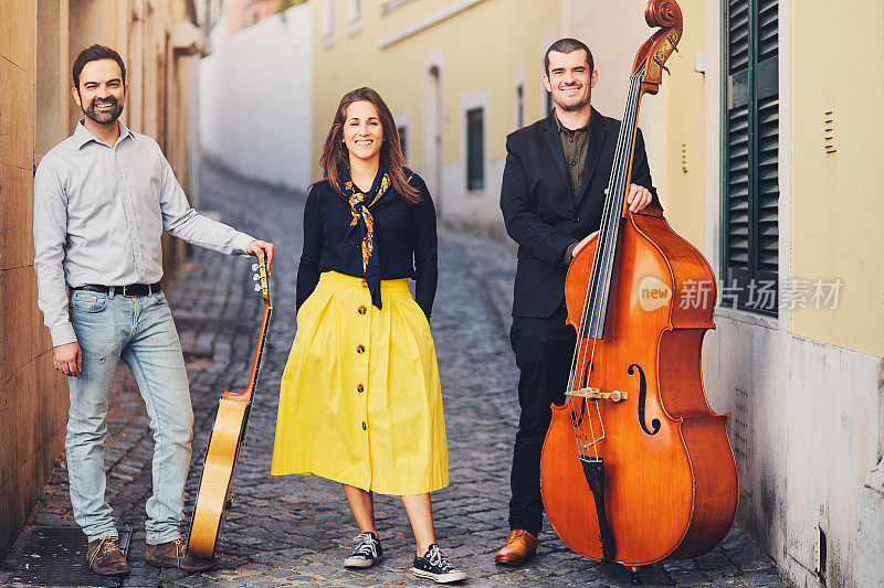 在一条古老的欧洲街道上，三个人组成的音乐团体。乐队由两个男人和一个女孩组成。男人用低音提琴和吉他。非传统的有创造力的人与乐器。