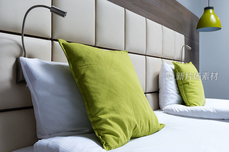 现代卧室的绿色枕头、阅读灯、皮革床头板