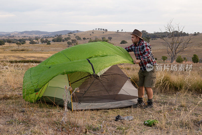 一个穿着法兰绒和牛仔帽的徒步旅行者把防水罩放在他的帐篷上