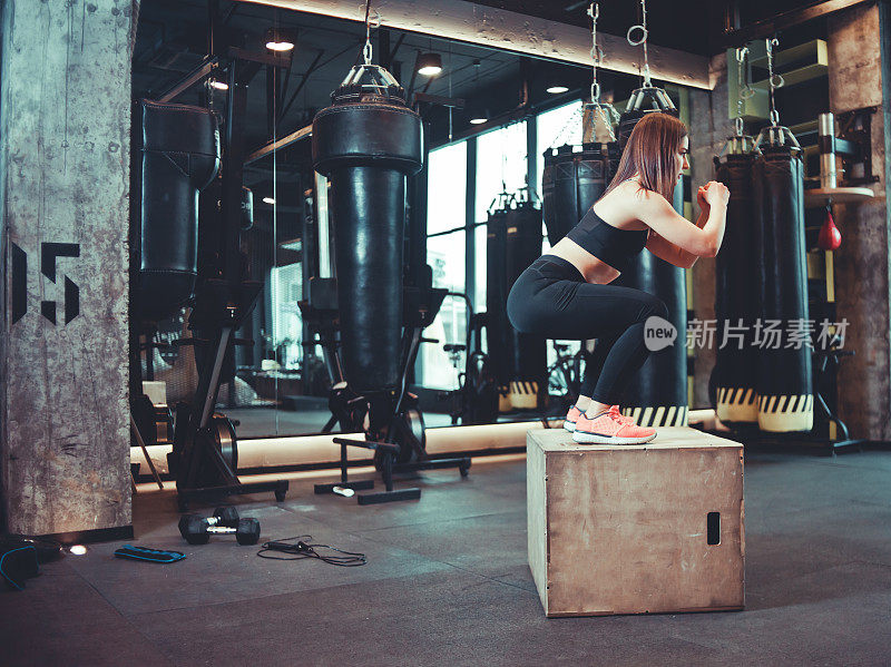 健身女跳上木箱在健身房训练，锻炼。穿着运动服的黑发女孩在健身房做跳跃运动