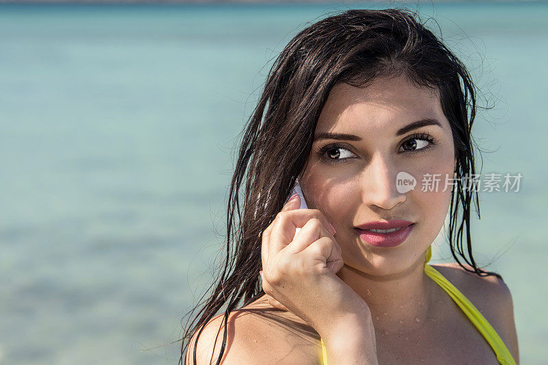黑头发的拉丁裔女孩对着大海背景上的手机说话