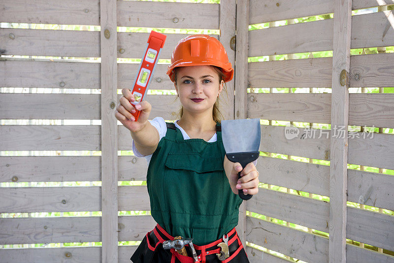 妇女与测量水平工具在建筑工地。妇女测量木墙和摆姿势的相机