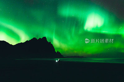 在冰岛山景城美丽的海滩上享受北极光的女人剪影